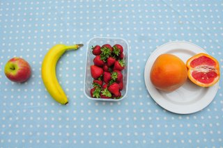 An apple, banana, punnet of strawberries, and a 1 and a half grapefruits on a table