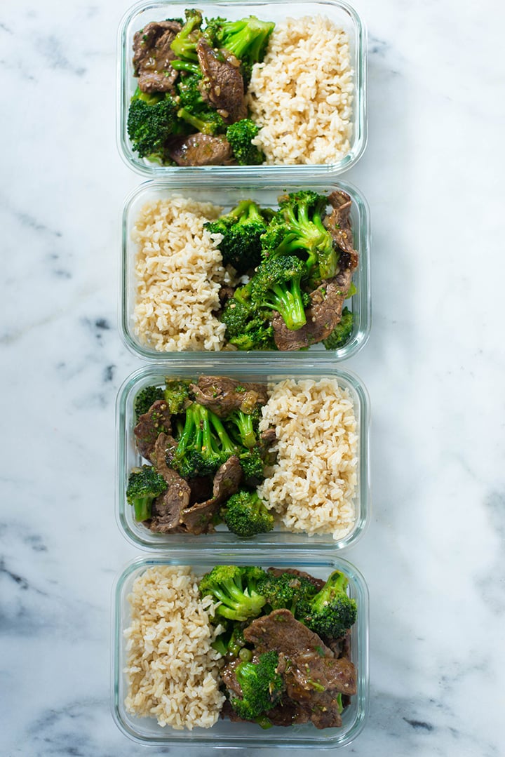 Overview of one of the dinners for the meal prep for weight loss, which is healthy beef and broccoli, organized and divided into four meal prep containers, next to brown rice, ready to refrigerate in meal prep containers.